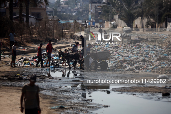 Palestinians are walking past sewage water and a garbage dump on a street in Deir el-Balah in the central Gaza Strip, on July 23, 2024, as m...