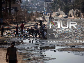 Palestinians are walking past sewage water and a garbage dump on a street in Deir el-Balah in the central Gaza Strip, on July 23, 2024, as m...