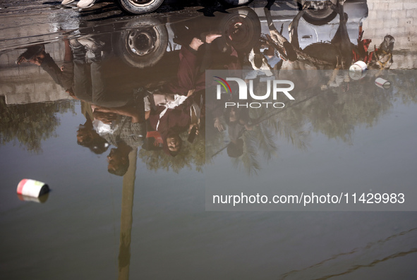 Palestinians are walking past a pool of sewage water on a street in Deir el-Balah in the central Gaza Strip on July 23, 2024, as municipal i...