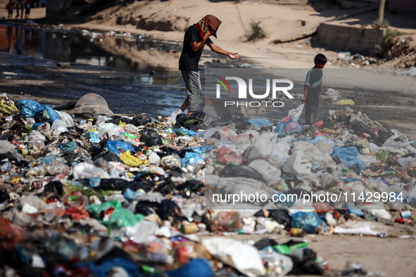 Palestinians are walking past sewage water and a garbage dump on a street in Deir el-Balah in the central Gaza Strip, on July 23, 2024, as m...