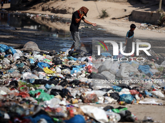 Palestinians are walking past sewage water and a garbage dump on a street in Deir el-Balah in the central Gaza Strip, on July 23, 2024, as m...