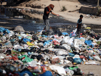 Palestinians are walking past sewage water and a garbage dump on a street in Deir el-Balah in the central Gaza Strip, on July 23, 2024, as m...