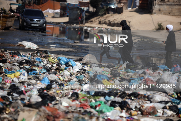 Palestinians are walking past sewage water and a garbage dump on a street in Deir el-Balah in the central Gaza Strip, on July 23, 2024, as m...