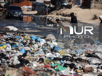 Palestinians are walking past sewage water and a garbage dump on a street in Deir el-Balah in the central Gaza Strip, on July 23, 2024, as m...