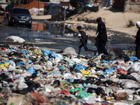 Palestinians are walking past sewage water and a garbage dump on a street in Deir el-Balah in the central Gaza Strip, on July 23, 2024, as m...