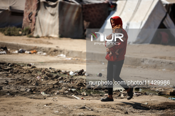 Palestinians are walking past a pool of sewage water on a street in Deir el-Balah in the central Gaza Strip on July 23, 2024, as municipal i...