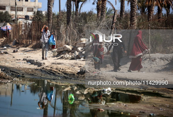 Palestinians are walking past a pool of sewage water on a street in Deir el-Balah in the central Gaza Strip on July 23, 2024, as municipal i...