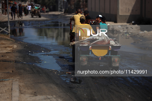 Palestinians are walking past a pool of sewage water on a street in Deir el-Balah in the central Gaza Strip on July 23, 2024, as municipal i...