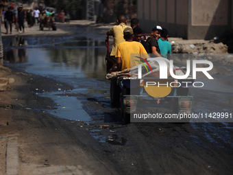 Palestinians are walking past a pool of sewage water on a street in Deir el-Balah in the central Gaza Strip on July 23, 2024, as municipal i...