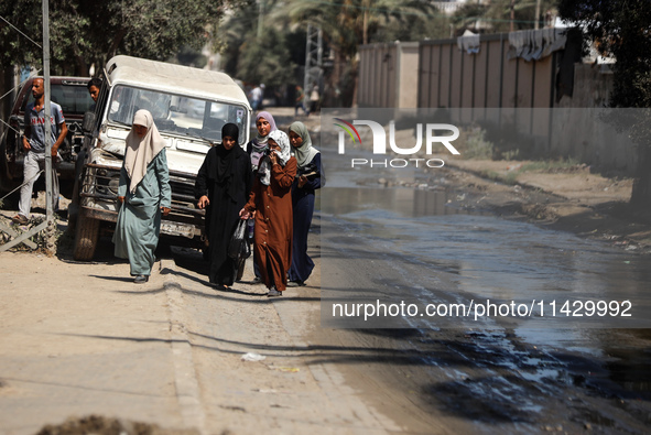 Palestinians are walking past a pool of sewage water on a street in Deir el-Balah in the central Gaza Strip on July 23, 2024, as municipal i...