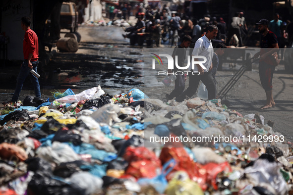 Palestinians are walking past sewage water and a garbage dump on a street in Deir el-Balah in the central Gaza Strip, on July 23, 2024, as m...