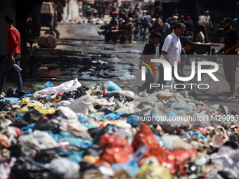 Palestinians are walking past sewage water and a garbage dump on a street in Deir el-Balah in the central Gaza Strip, on July 23, 2024, as m...