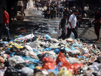 Palestinians are walking past sewage water and a garbage dump on a street in Deir el-Balah in the central Gaza Strip, on July 23, 2024, as m...