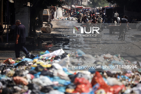 Palestinians are walking past sewage water and a garbage dump on a street in Deir el-Balah in the central Gaza Strip, on July 23, 2024, as m...