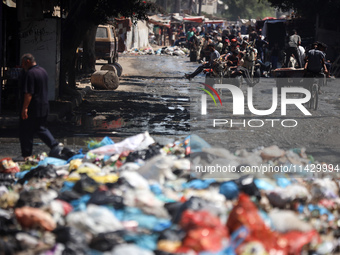 Palestinians are walking past sewage water and a garbage dump on a street in Deir el-Balah in the central Gaza Strip, on July 23, 2024, as m...