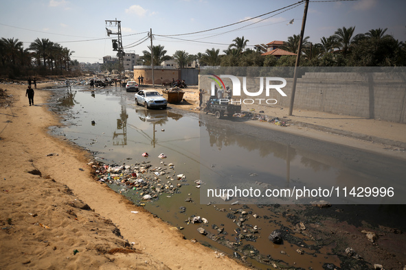 Palestinians are walking past a pool of sewage water on a street in Deir el-Balah in the central Gaza Strip on July 23, 2024, as municipal i...