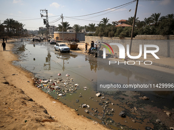 Palestinians are walking past a pool of sewage water on a street in Deir el-Balah in the central Gaza Strip on July 23, 2024, as municipal i...