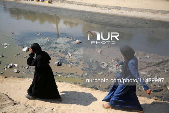 Palestinians are walking past a pool of sewage water on a street in Deir el-Balah in the central Gaza Strip on July 23, 2024, as municipal i...