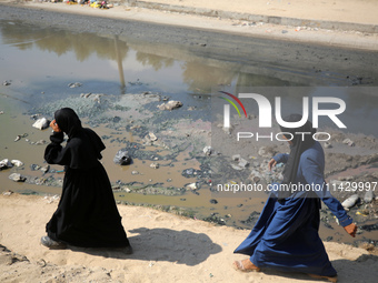 Palestinians are walking past a pool of sewage water on a street in Deir el-Balah in the central Gaza Strip on July 23, 2024, as municipal i...