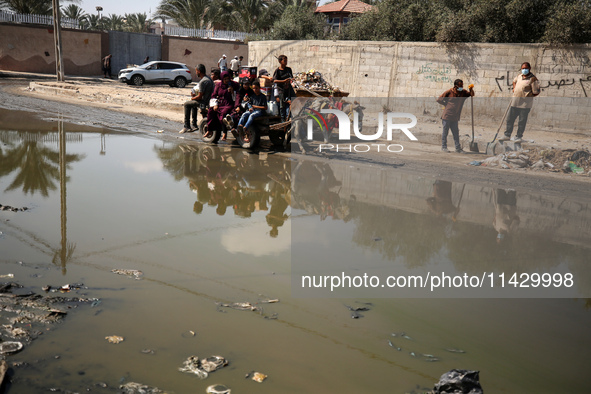 Palestinians are walking past a pool of sewage water on a street in Deir el-Balah in the central Gaza Strip on July 23, 2024, as municipal i...