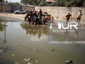 Palestinians are walking past a pool of sewage water on a street in Deir el-Balah in the central Gaza Strip on July 23, 2024, as municipal i...