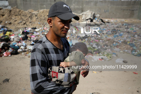 Palestinians are walking past sewage water and a garbage dump on a street in Deir el-Balah in the central Gaza Strip, on July 23, 2024, as m...