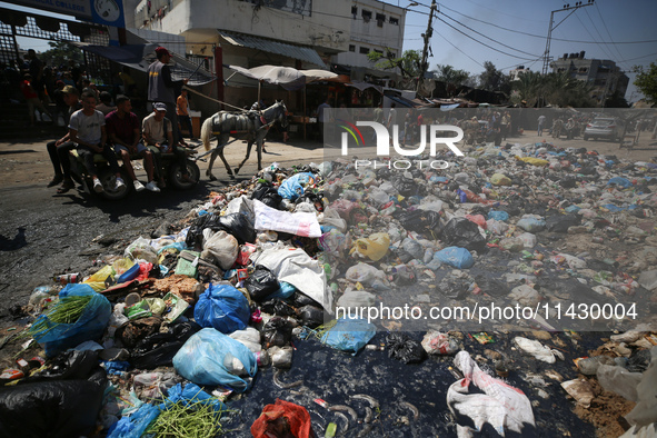 Palestinians are riding a donkey-drawn cart past a garbage dump and sewage water on a street in Deir el-Balah in the central Gaza Strip, on...