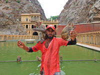 A man is standing with macaques near the holy pond 'Kund' of Shrine Galta Peeth Tirtha, also famous as 'Galta Ji temple' and 'Monkey temple'...