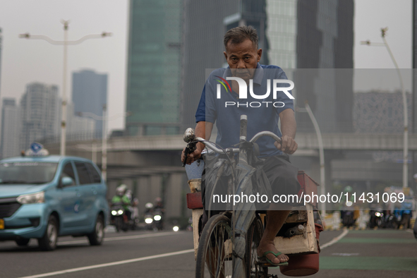 A man is cycling across a road in the central business district of Jakarta, Indonesia, on July 24, 2024. 