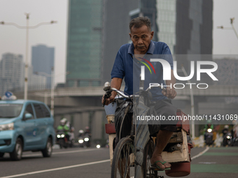 A man is cycling across a road in the central business district of Jakarta, Indonesia, on July 24, 2024. (