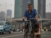 A man is cycling across a road in the central business district of Jakarta, Indonesia, on July 24, 2024. (