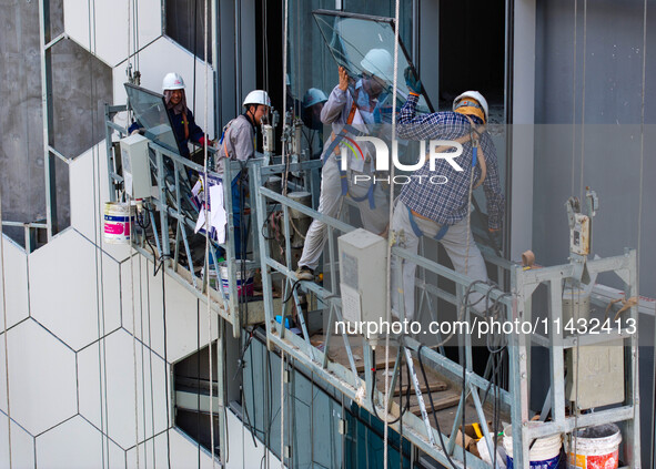 Workers are installing a glass curtain wall outside a high-rise building in Huai'an, China, on July 25, 2024. 