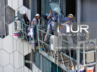 Workers are installing a glass curtain wall outside a high-rise building in Huai'an, China, on July 25, 2024. (