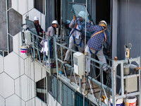 Workers are installing a glass curtain wall outside a high-rise building in Huai'an, China, on July 25, 2024. (