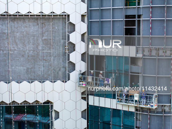 Workers are installing a glass curtain wall outside a high-rise building in Huai'an, China, on July 25, 2024. 