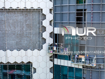 Workers are installing a glass curtain wall outside a high-rise building in Huai'an, China, on July 25, 2024. (