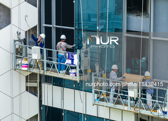 Workers are installing a glass curtain wall outside a high-rise building in Huai'an, China, on July 25, 2024. 