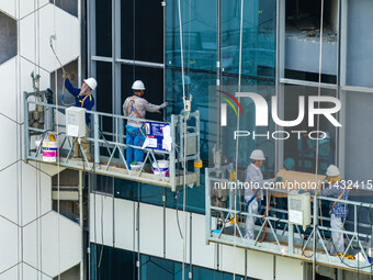 Workers are installing a glass curtain wall outside a high-rise building in Huai'an, China, on July 25, 2024. (