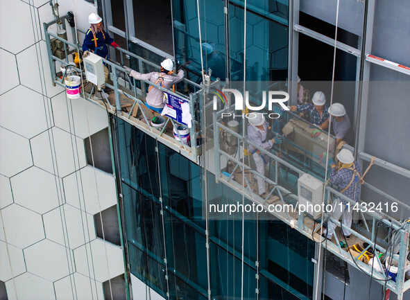 Workers are installing a glass curtain wall outside a high-rise building in Huai'an, China, on July 25, 2024. 