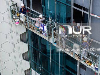 Workers are installing a glass curtain wall outside a high-rise building in Huai'an, China, on July 25, 2024. (