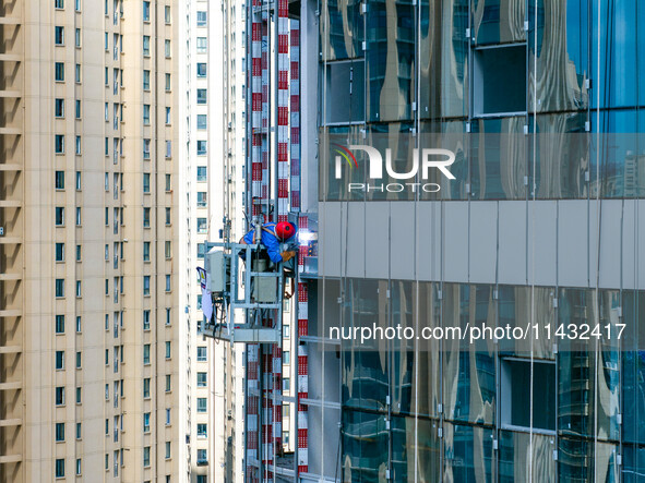 Workers are installing a glass curtain wall outside a high-rise building in Huai'an, China, on July 25, 2024. 