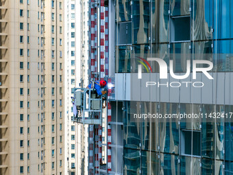 Workers are installing a glass curtain wall outside a high-rise building in Huai'an, China, on July 25, 2024. (