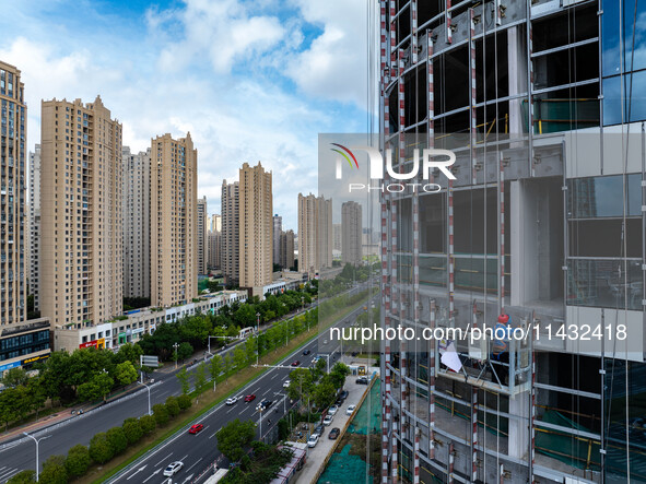 Workers are installing a glass curtain wall outside a high-rise building in Huai'an, China, on July 25, 2024. 