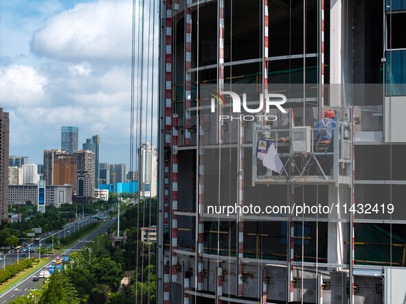 Workers are installing a glass curtain wall outside a high-rise building in Huai'an, China, on July 25, 2024. 