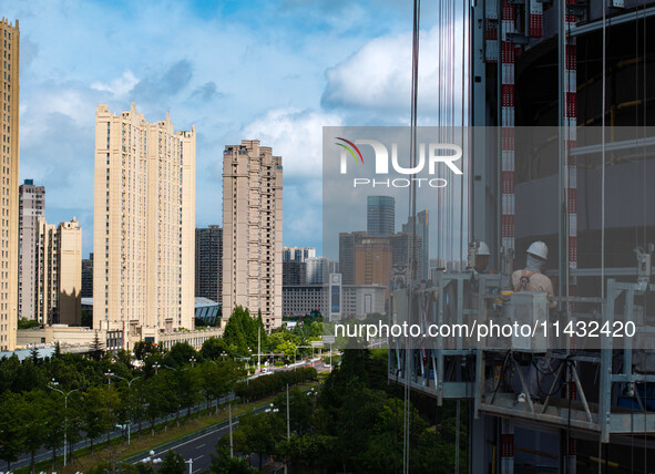 Workers are installing a glass curtain wall outside a high-rise building in Huai'an, China, on July 25, 2024. 