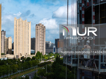 Workers are installing a glass curtain wall outside a high-rise building in Huai'an, China, on July 25, 2024. (