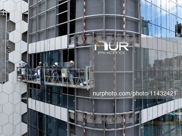 Workers are installing a glass curtain wall outside a high-rise building in Huai'an, China, on July 25, 2024. 