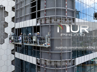 Workers are installing a glass curtain wall outside a high-rise building in Huai'an, China, on July 25, 2024. (