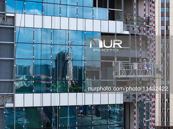 Workers are installing a glass curtain wall outside a high-rise building in Huai'an, China, on July 25, 2024. 