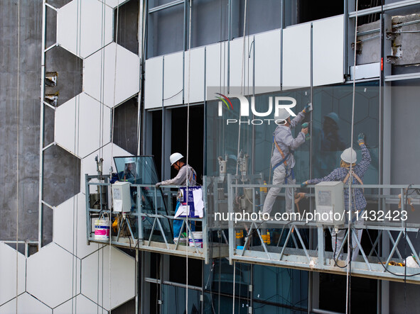 Workers are installing a glass curtain wall outside a high-rise building in Huai'an, China, on July 25, 2024. 